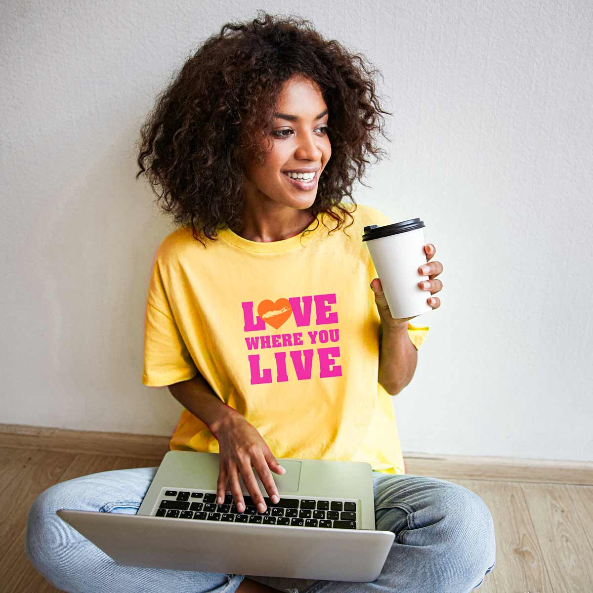 Beautiful African American woman sitting and working while wearing yellow love where you live Long Island shirt